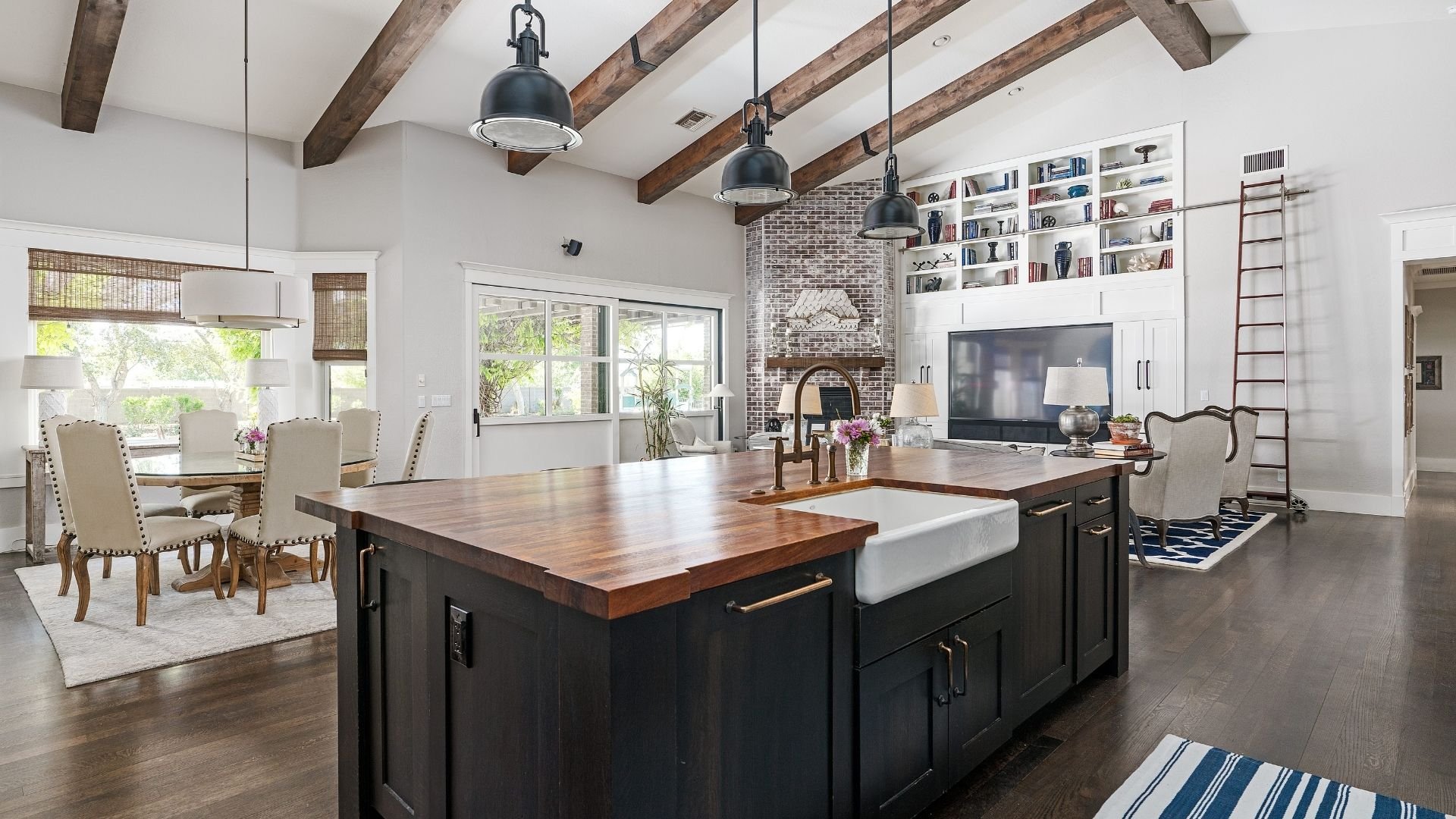 Modern open-concept kitchen and living room with exposed wood beams and black pendant lights.