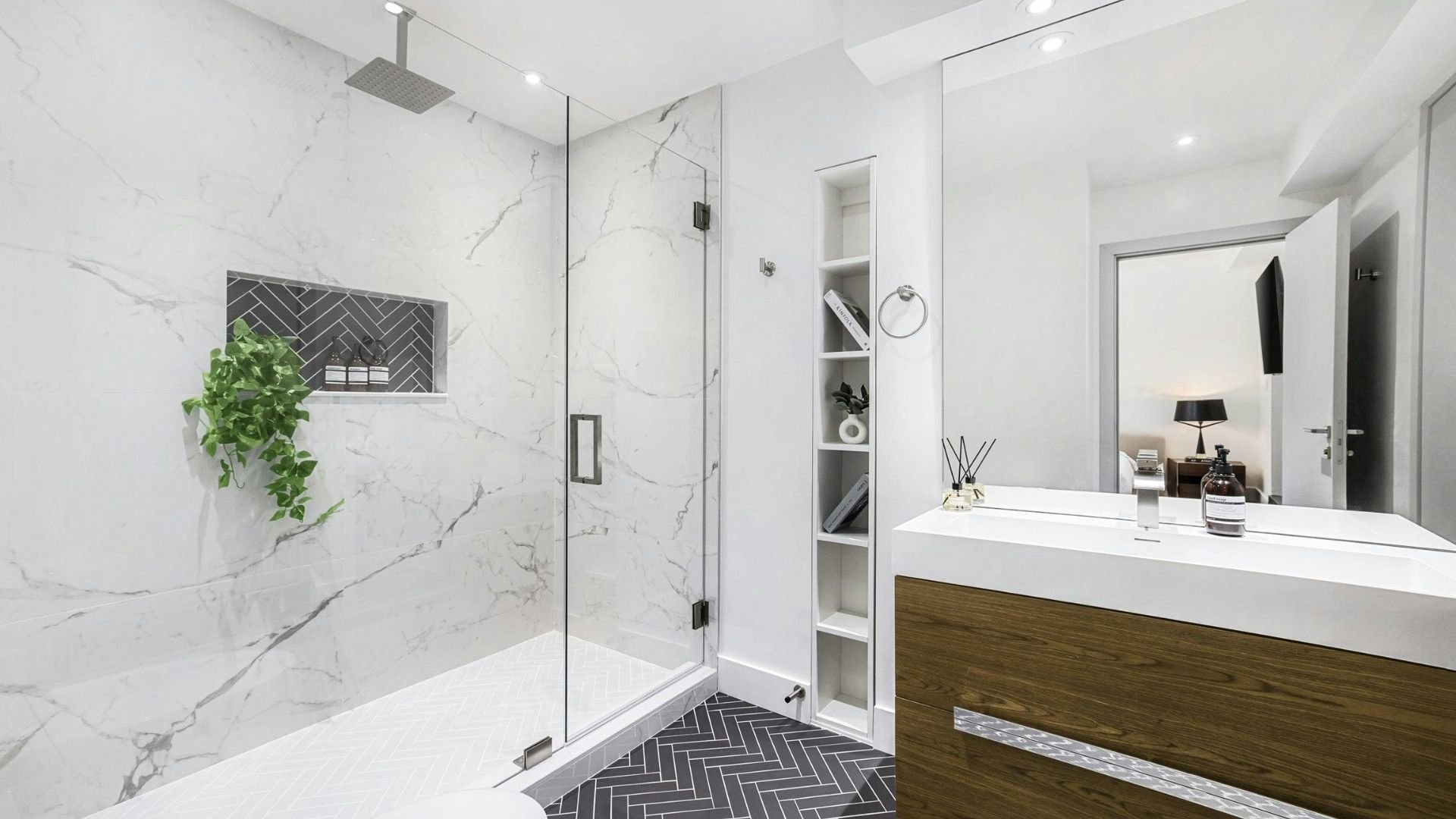 Modern luxury bathroom with marble walls, glass shower, white vanity, and built-in shelving.